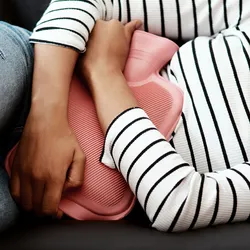 Photo of a pregnant woman lying on her side and holding a hot water bottle to her abdomen.