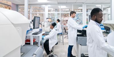 Photo of a multiracial team of clinical laboratory scientists wearing PPE and working in a CLIA-certified laboratory environment on companion diagnostics.