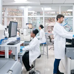 Photo of a multiracial team of clinical laboratory scientists wearing PPE and working in a CLIA-certified laboratory environment on companion diagnostics.