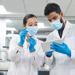 Two clinical laboratory scientists wearing PPE in the laboratory hold a clipboard and review the milestones toward the new FDA LDT Final Rule.