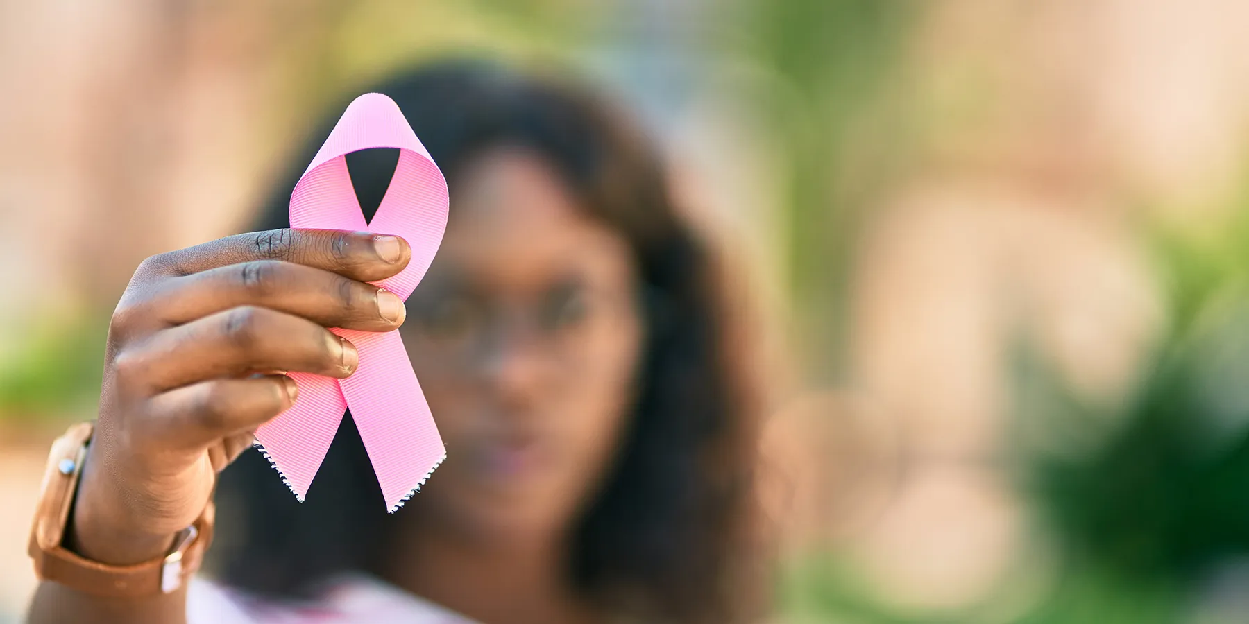 Photo of a Black woman in the background holding up a pink ribbon to represent breast cancer awareness.