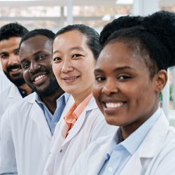 Photo of a diverse group of five laboratorians wearing white lab coats in a clinical laboratory and smiling at the camera.