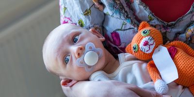 Photo of a white hospital nurse holding a white baby conceived via in vitro fertilization with a soother in its mouth in her arms.
