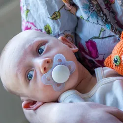 Photo of a white hospital nurse holding a white baby conceived via in vitro fertilization with a soother in its mouth in her arms.