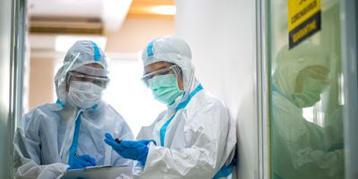 Photo of two infectious disease researchers wearing full PPE examining a sample from a COVID-19 patient. caption: