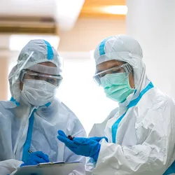 Photo of two infectious disease researchers wearing full PPE examining a sample from a COVID-19 patient. caption: