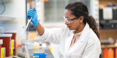 Photo of clinical laboratory professional wearing PPE and pipetting biomarker samples at a laboratory bench.