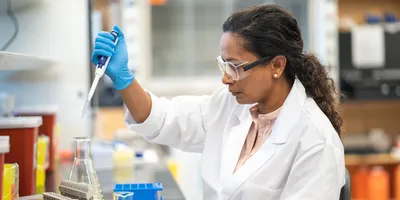 Photo of clinical laboratory professional wearing PPE and pipetting biomarker samples at a laboratory bench.