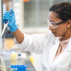 Photo of clinical laboratory professional wearing PPE and pipetting biomarker samples at a laboratory bench.