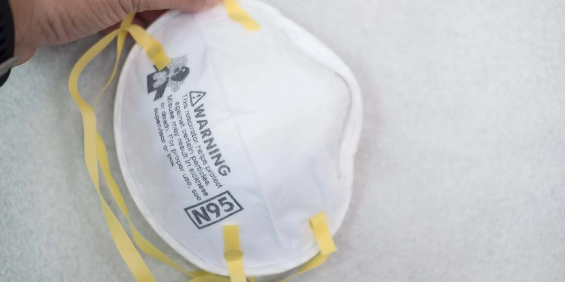 Photo of a white N95 face mask with yellow straps against a white background.
