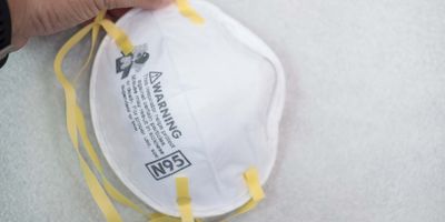 Photo of a white N95 face mask with yellow straps against a white background.