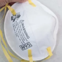 Photo of a white N95 face mask with yellow straps against a white background.