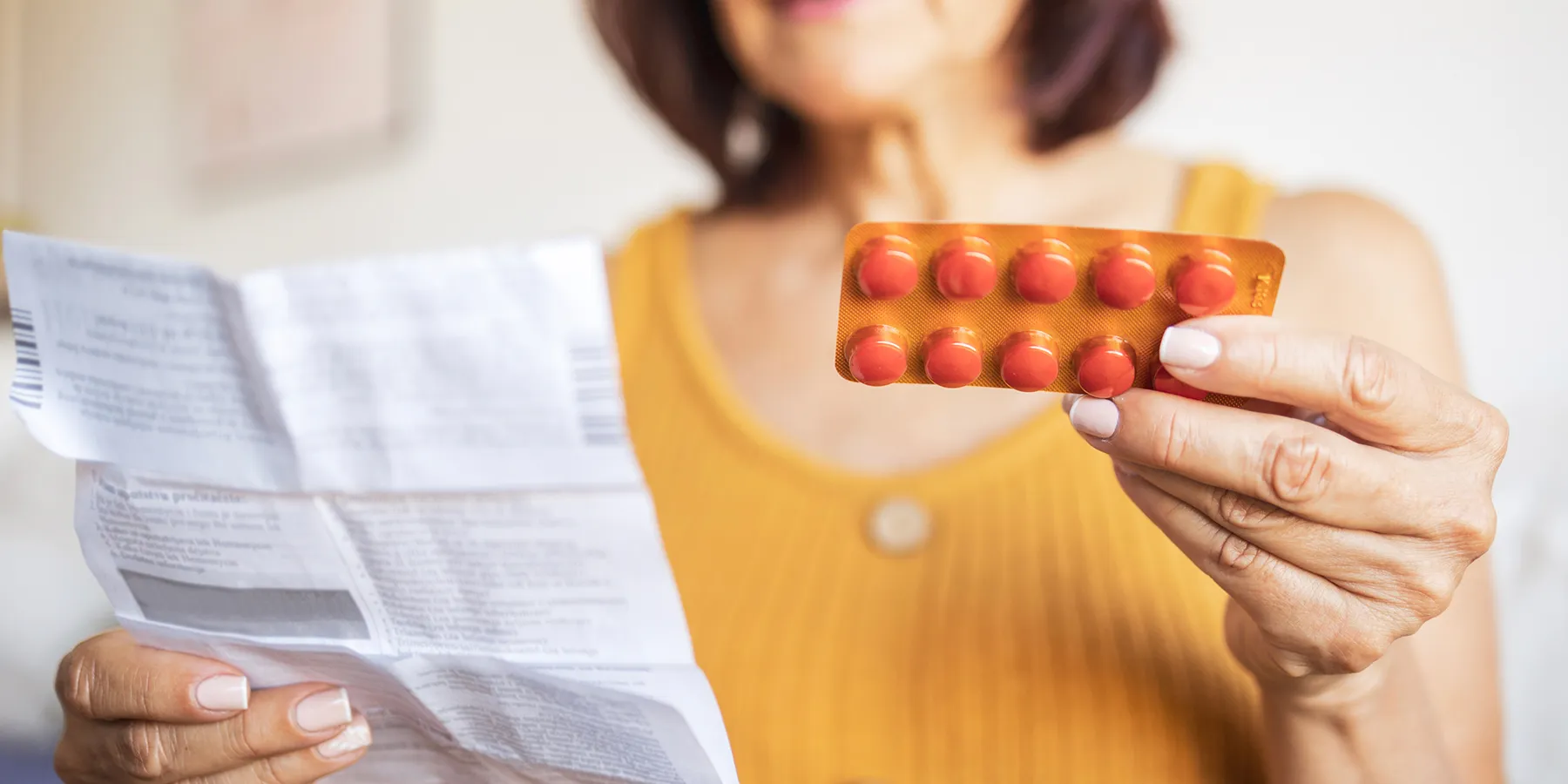 Photo of a white woman holding a blister package of omega-3 and omega-6 fatty acid supplements in her hand.