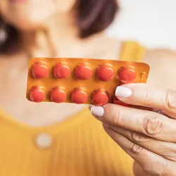 Photo of a white woman holding a blister package of omega-3 and omega-6 fatty acid supplements in her hand.
