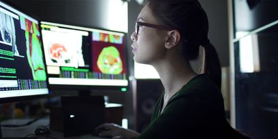 Photo of a female clinician researcher sitting at multiple computer screens while examining physiological data from patients’ breath chemistry.