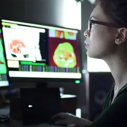 Photo of a female clinician researcher sitting at multiple computer screens while examining physiological data from patients’ breath chemistry.
