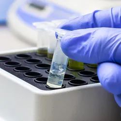 Photo of a clinical lab professional’s gloved hand holding a small clear tube of exosomes and extracellular vesicles in the laboratory.