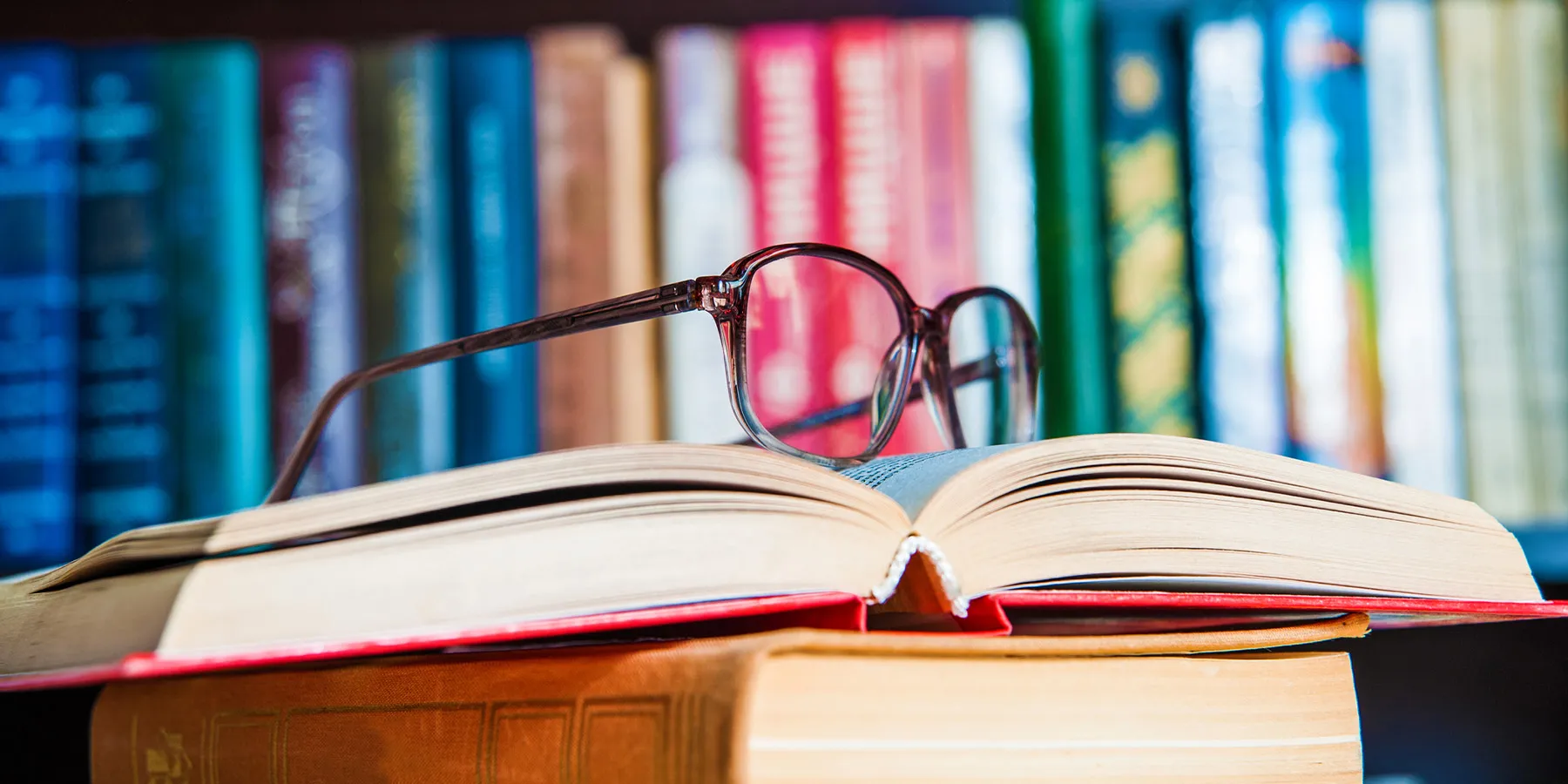 Photo of a pair of black eye glasses on top of an open book inside of a library.