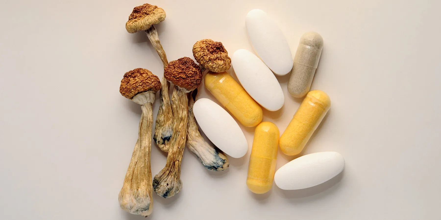 Photo of dried psilocybin mushrooms and psilocybin capsules and pills against a white background.
