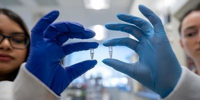 Photo of two McMaster researchers wearing gloves holding up two samples of the bacteriophages used in the new lab test.