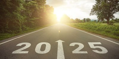 Photo of the number ‘2025’ and an arrow pointed forward into the distance painted on a road at sunset. 