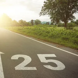 Photo of the number ‘2025’ and an arrow pointed forward into the distance painted on a road at sunset. 