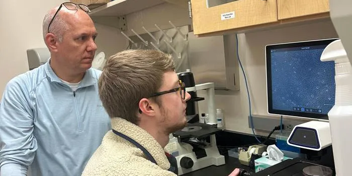 Photo of Kirk Staschke and Noah Sommers, a PhD student at the IU School of Medicine, at the microscope.