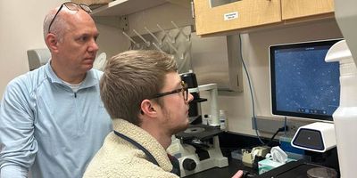 Photo of Kirk Staschke and Noah Sommers, a PhD student at the IU School of Medicine, at the microscope.