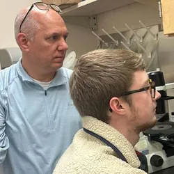 Photo of Kirk Staschke and Noah Sommers, a PhD student at the IU School of Medicine, at the microscope.