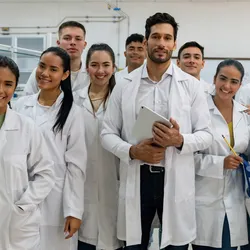 Photo of a group scientists wearing white lab coats standing in a laboratory and smiling at the camera.
