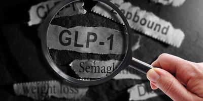Photo of someone holding a magnifying glass over the word “GLP-1” against a black background.