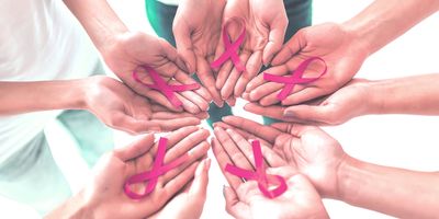 Photo of a circle of human hands holding pink breast cancer awareness ribbons in their palms.