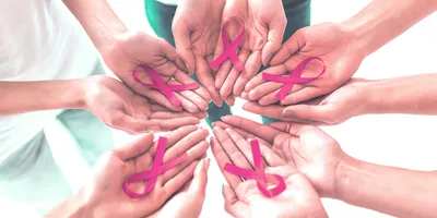 Photo of a circle of human hands holding pink breast cancer awareness ribbons in their palms.