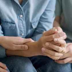 Photo of a person’s hands as they are comforted by another while they undergo a clinic visit for kidney transplant evaluation and testing.