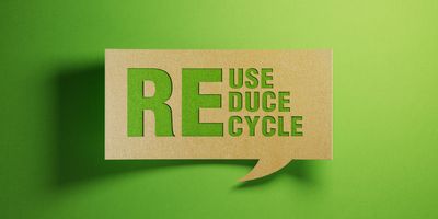 Photo of the words Reuse, Reduce, Recycle in green against a cardboard background representing sustainability practices.