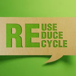 Photo of the words Reuse, Reduce, Recycle in green against a cardboard background representing sustainability practices.