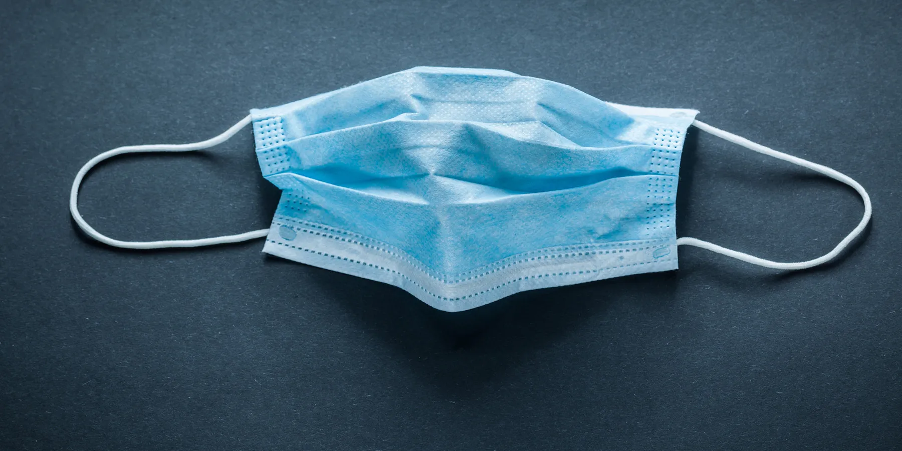 Photo of a blue surgical mask against a black background to represent the risk of COVID-19 infection in pregnancy.