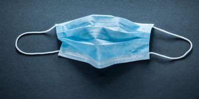 Photo of a blue surgical mask against a black background to represent the risk of COVID-19 infection in pregnancy.