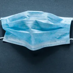 Photo of a blue surgical mask against a black background to represent the risk of COVID-19 infection in pregnancy.