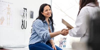 Photo of a young female cancer patient with long black hair in a health care setting shaking the hand of a healthcare provider conducting cancer screening.