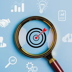 A magnifying glass focused on a target symbol with icons representing business development, strategy, implementation, lab testing, etc. around it on a blue background to represent an actionable strategy.