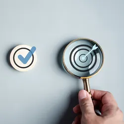 Photo of a person holding a magnifying glass over a target symbol to represent a checklist.