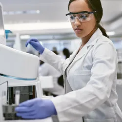 Photo of a clinical lab professional wearing a white lab coat and gloves in a clinical lab and loading a multiple sclerosis sample into an analyzer.
