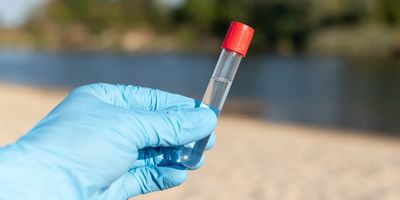 Photo of a laboratory scientist's gloved hand holding up a water sample from a river to be tested for antibiotics.