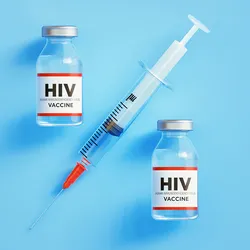 Photo of two HIV vaccine glass vials and a syringe against a light blue background.