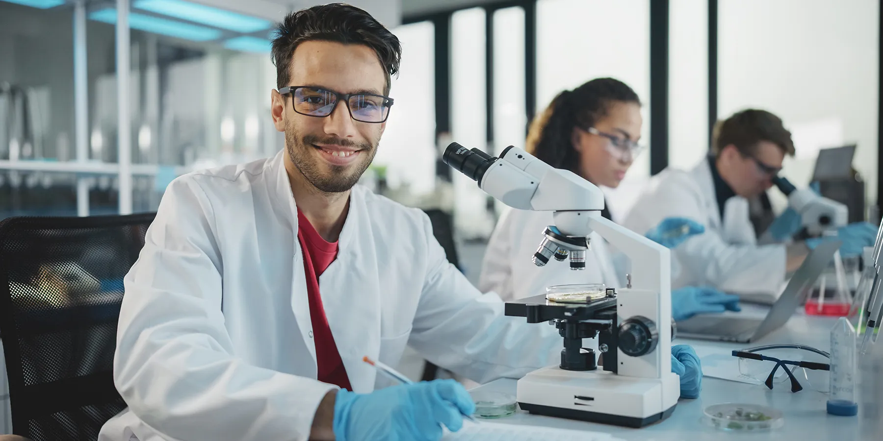 Photo of a clinical lab scientist wearing a white lab coat and blue gloves while analyzing samples for clinical bioinformatics in a medical laboratory.