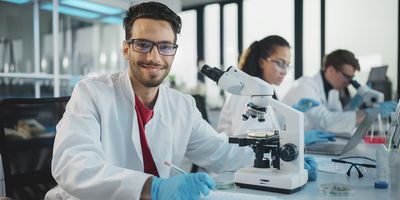 Photo of a clinical lab scientist wearing a white lab coat and blue gloves while analyzing samples for clinical bioinformatics in a medical laboratory.