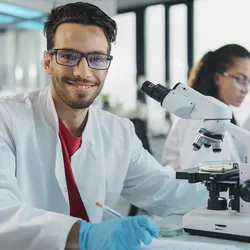 Photo of a clinical lab scientist wearing a white lab coat and blue gloves while analyzing samples for clinical bioinformatics in a medical laboratory.