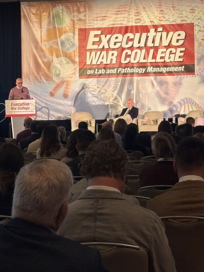 Dr. Joaquin Garcia presenting on a stage in a large conference hall during the Executive War College general session.