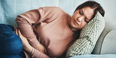 Woman experiencing abdominal discomfort on a couch due to gaps in follow-up testing.